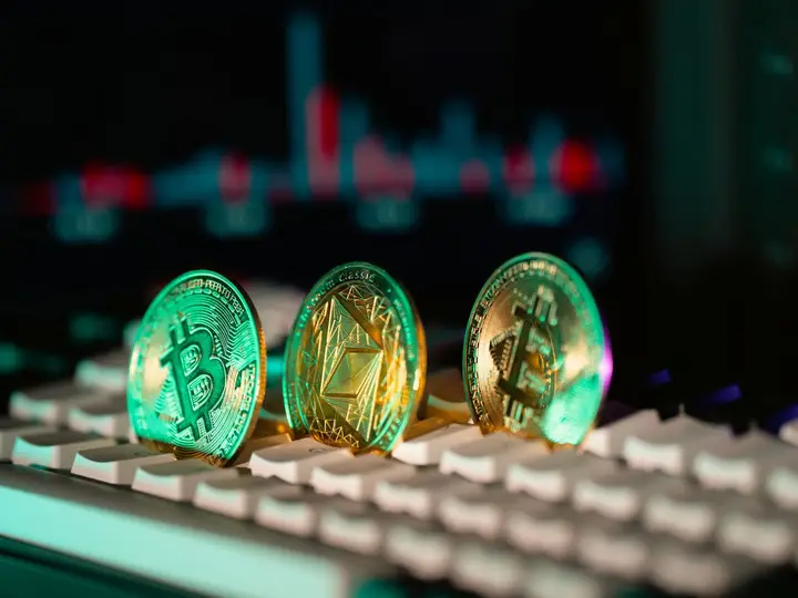 A bitcoin coin resting on a keyboard in front of a price chart