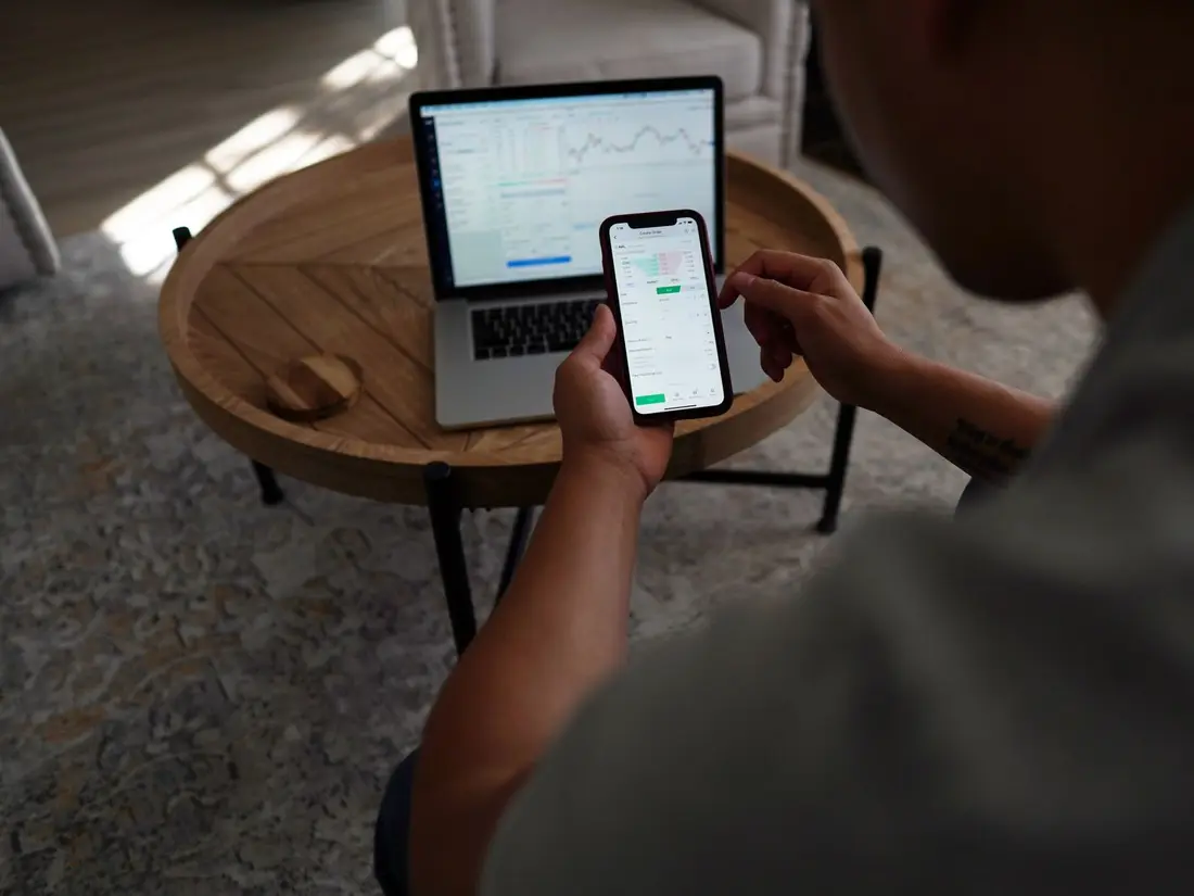 Someone checking a trading chart on a laptop and a phone